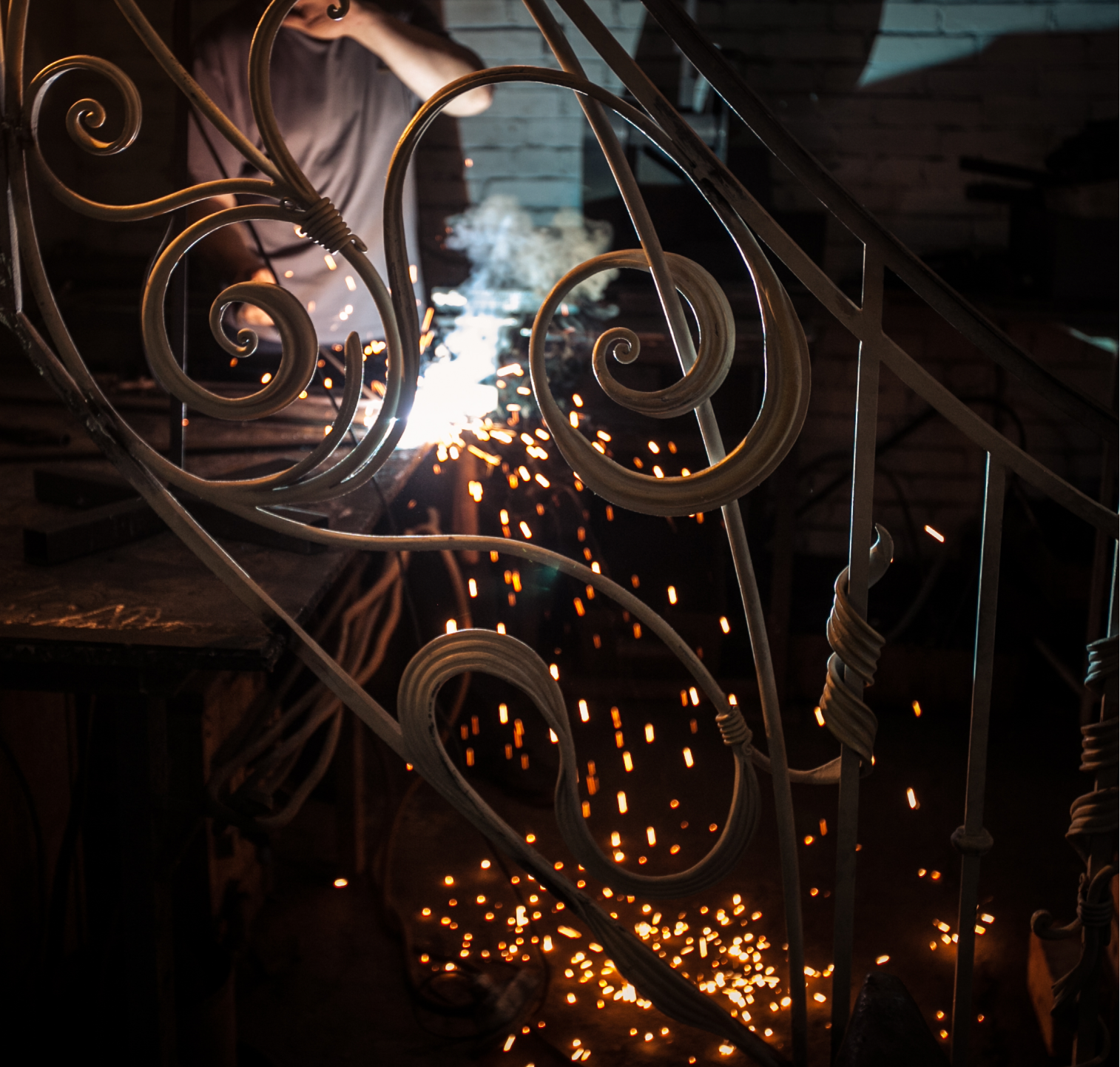 Sparks flying as a craftsman welds a scrolled wrought iron railing